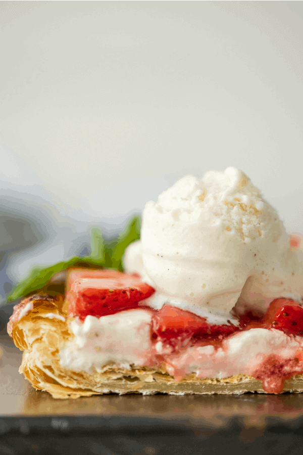 Close up of sliced puff pastry strawberry tart topped with a scoop of vanilla ice cream