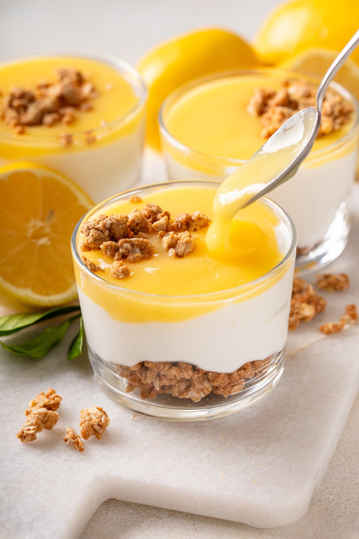 Lemon curd being spooned on top of a ramekin of cheesecake.