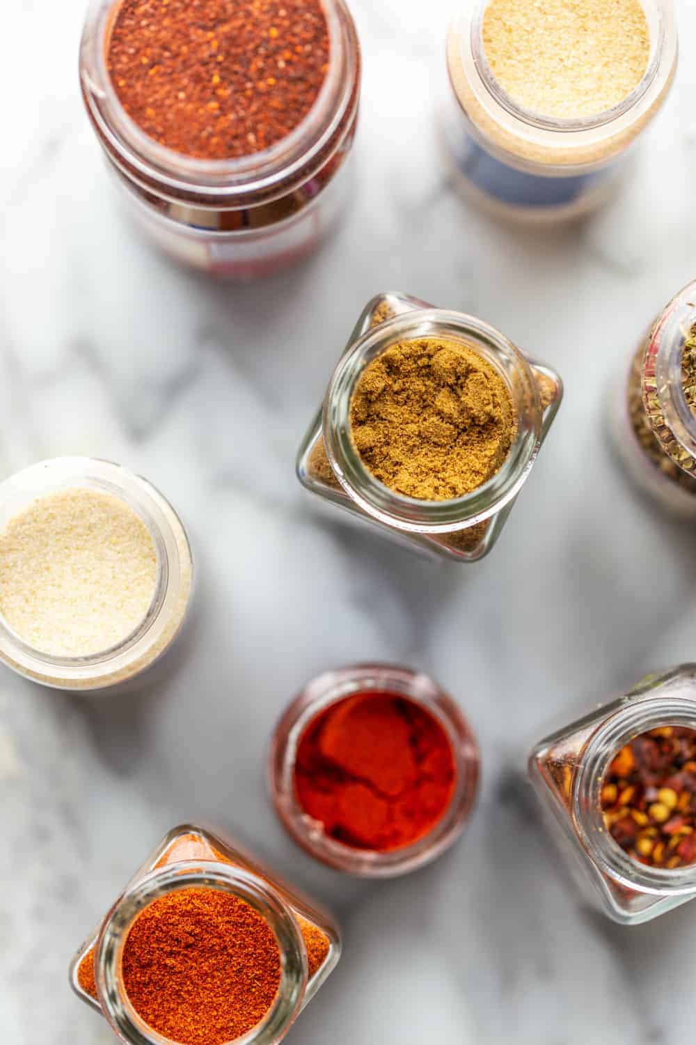 Overhead view of open spice jars for taco seasoning on a marble surface