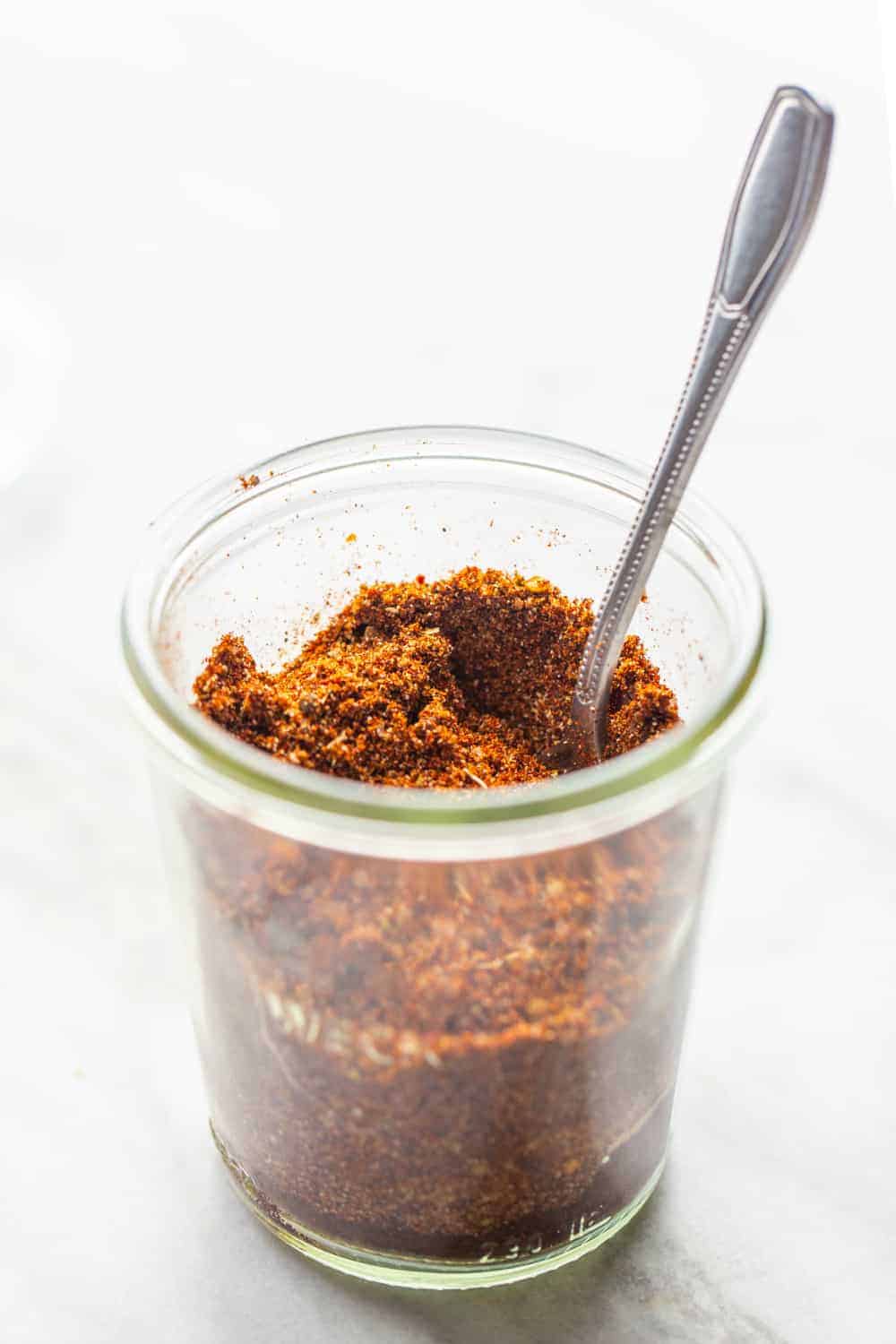 Side view of homemade chili seasoning in a jar with a spoon