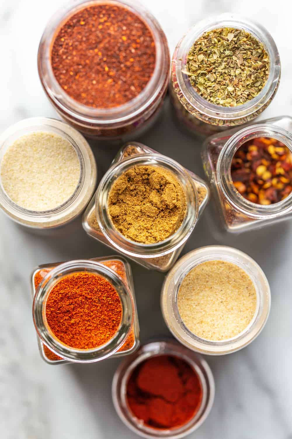 Overhead view of open spice jars for chili seasoning on marble surface