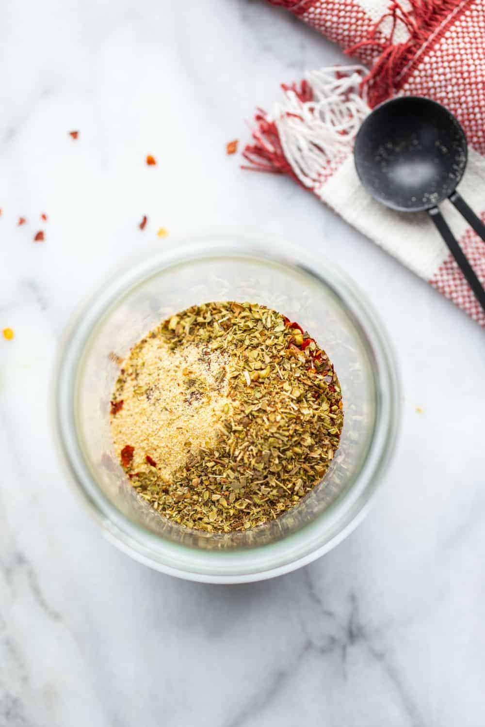 Open jar with spices for chili seasoning next to a measuring spoon