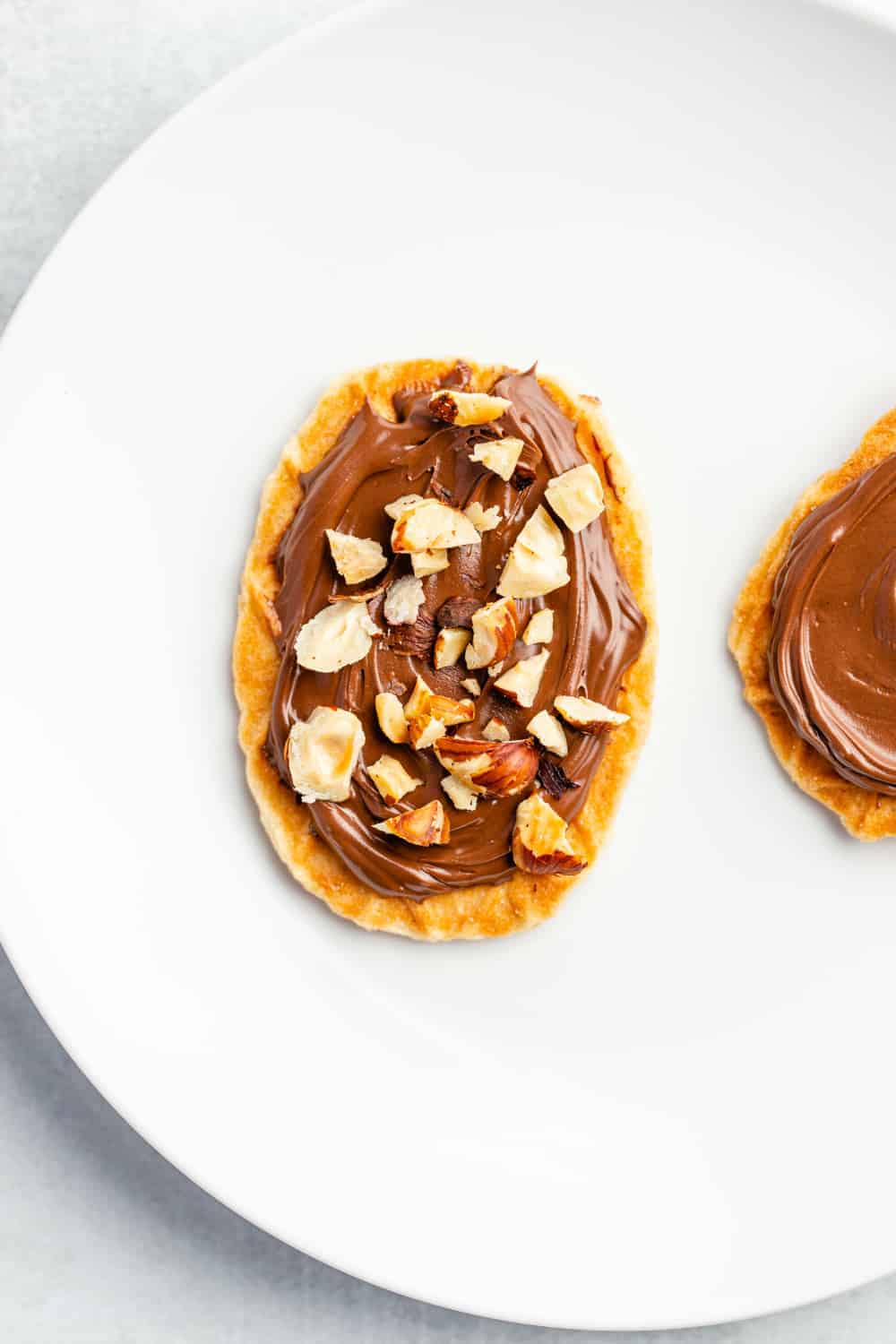 Overhead view of plated waffle cookie topped with chocolate hazelnut spread and chopped toasted hazelnuts