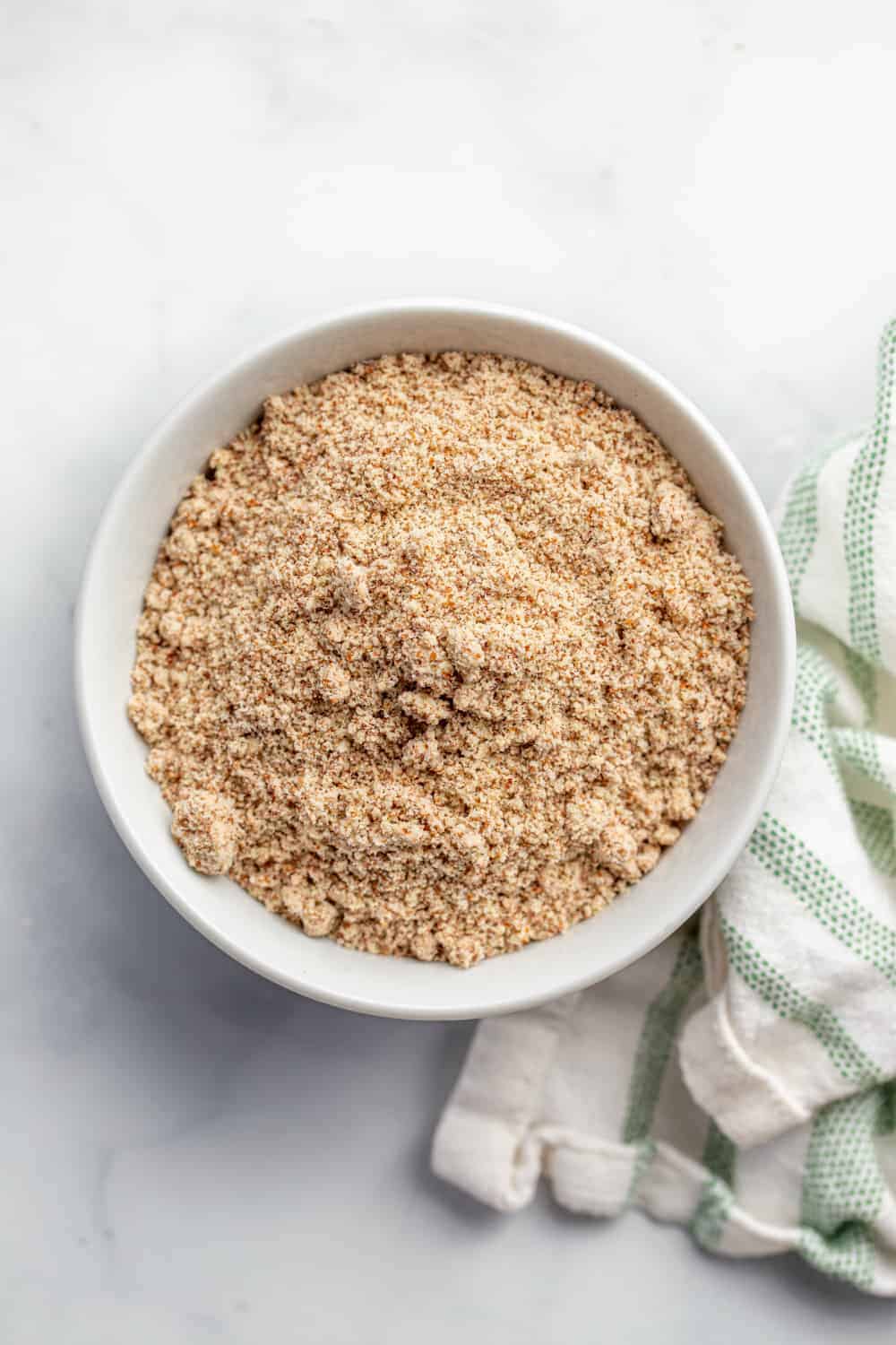 Finely ground almond meal in a white bowl next to a dish towel