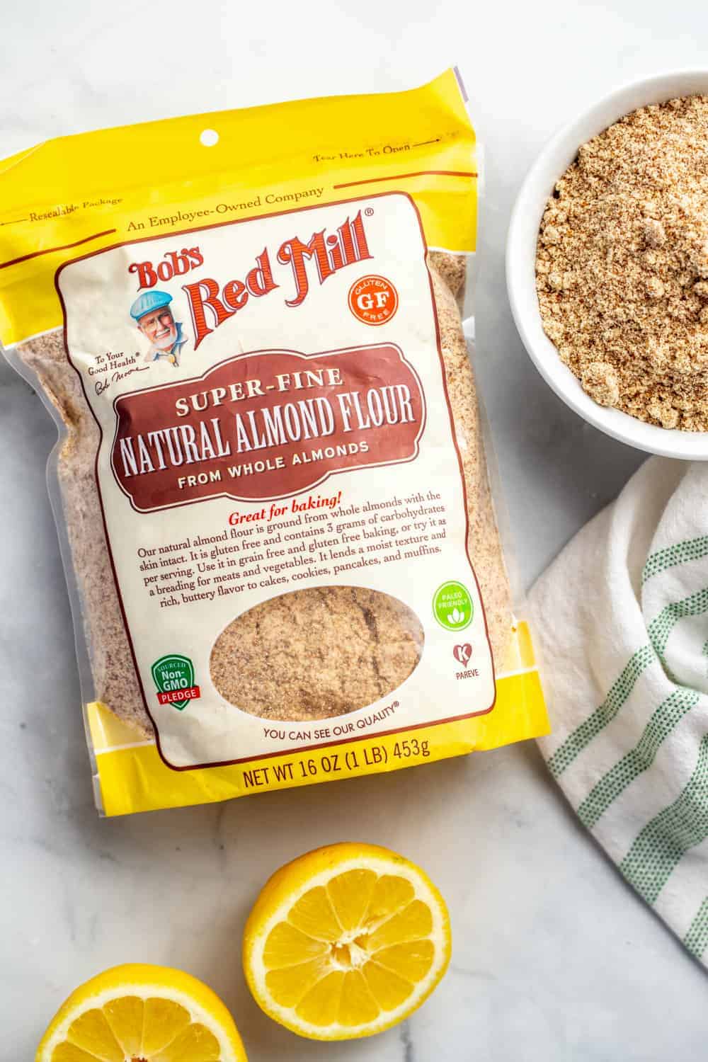 Bag of finely ground almond meal next to a bowl of almond meal and halved lemons