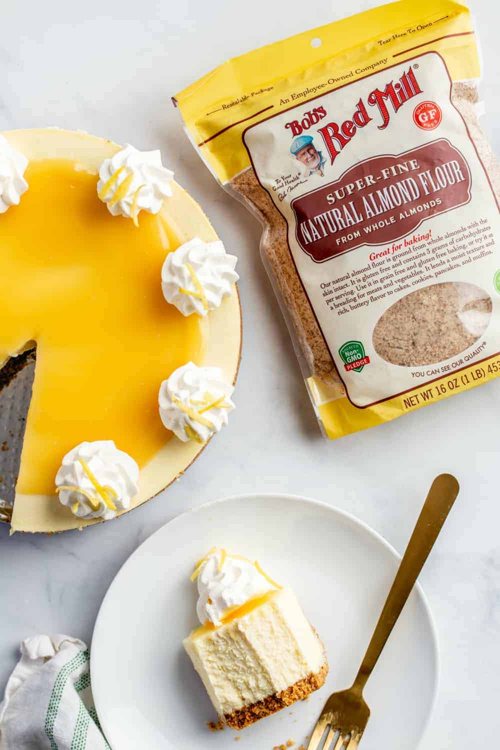 Lemon cheesecake next to a slice of lemon cheesecake and a bag of finely ground almond meal