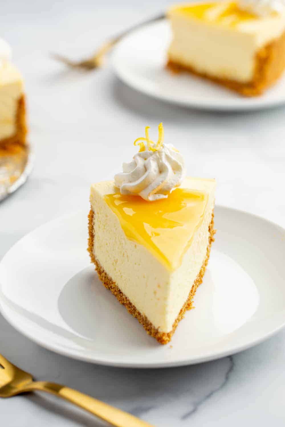 Front view of a slice of lemon cheesecake topped with lemon curd and whipped cream