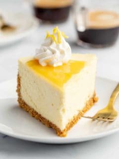 Plated slice of lemon cheesecake next to a fork with espresso in the background