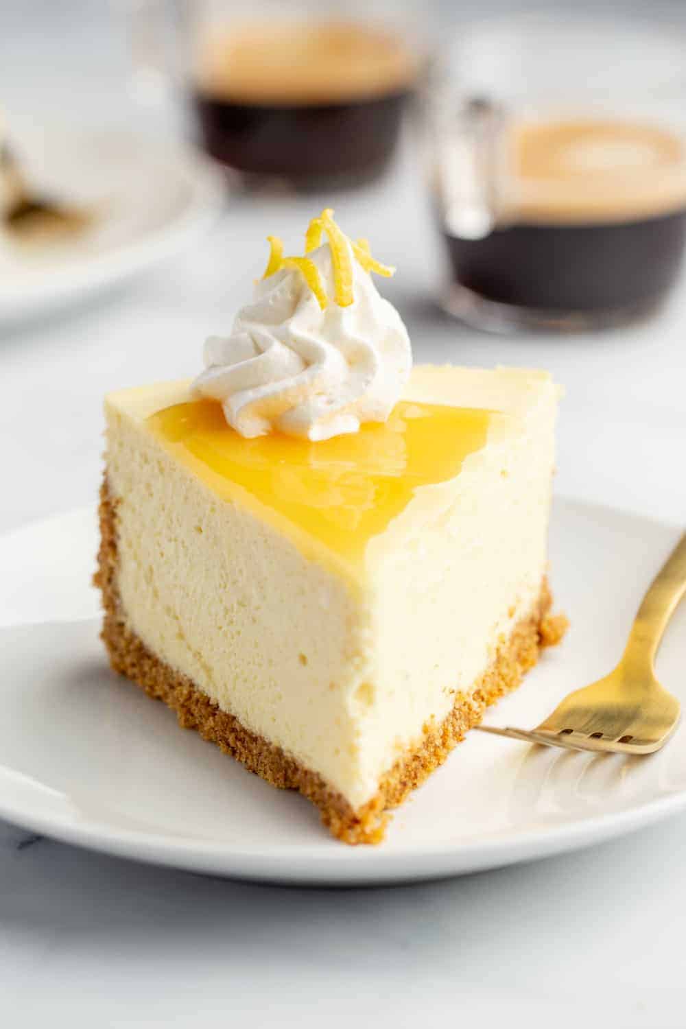 Plated slice of lemon cheesecake next to a fork with espresso in the background