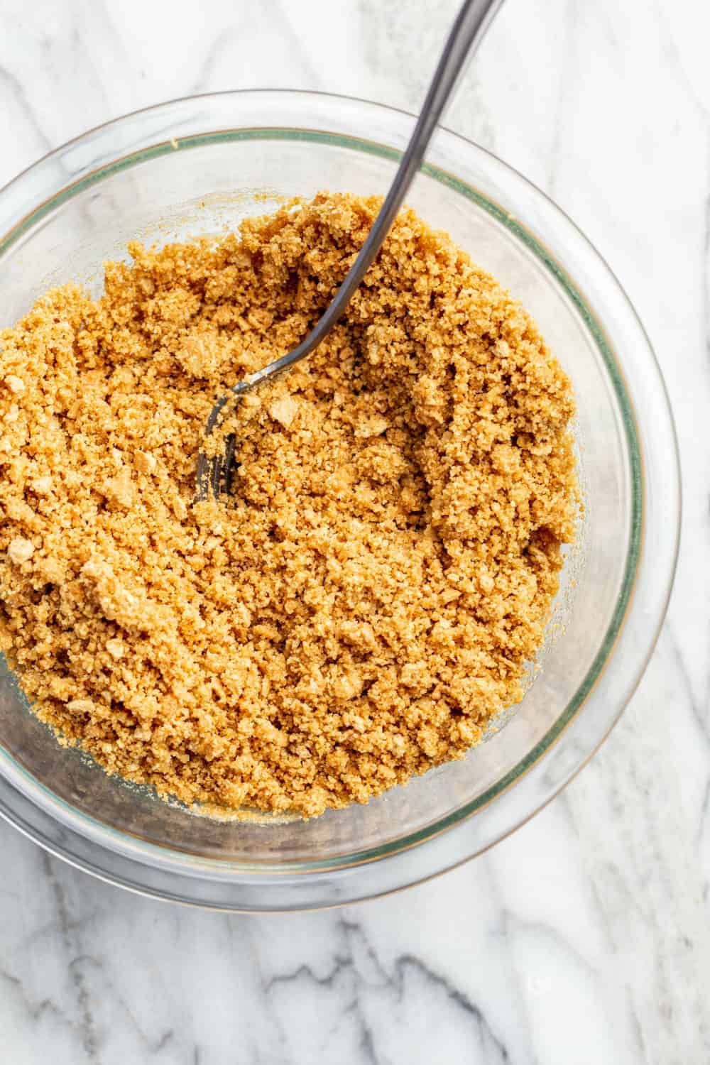 Graham cracker crust mixture in a glass bowl on a marble surface