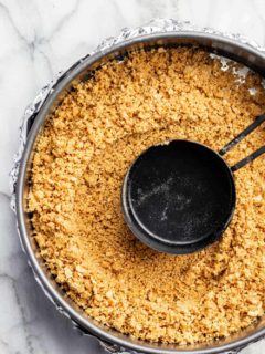 Measuring cup pressing mixture for graham cracker crust into a springform pan