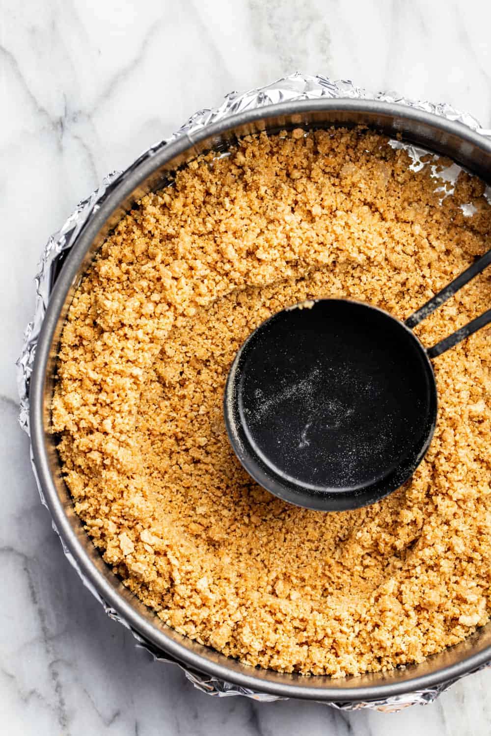 Measuring cup pressing mixture for graham cracker crust into a springform pan