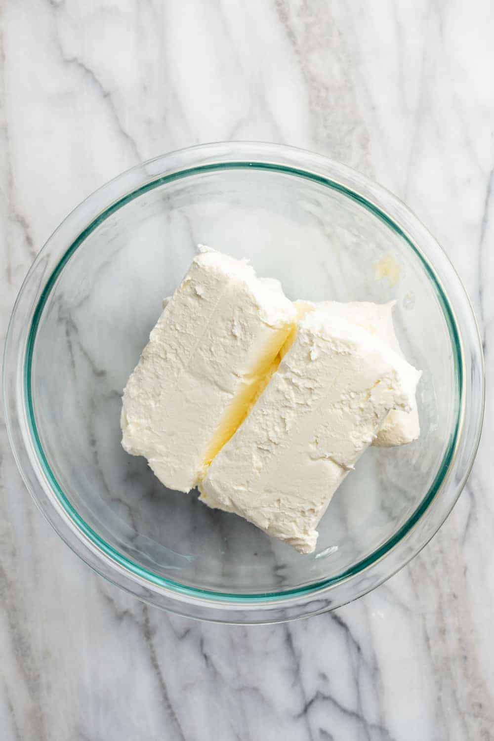 Blocks of softened cream cheese in a glass bowl on a marble surface