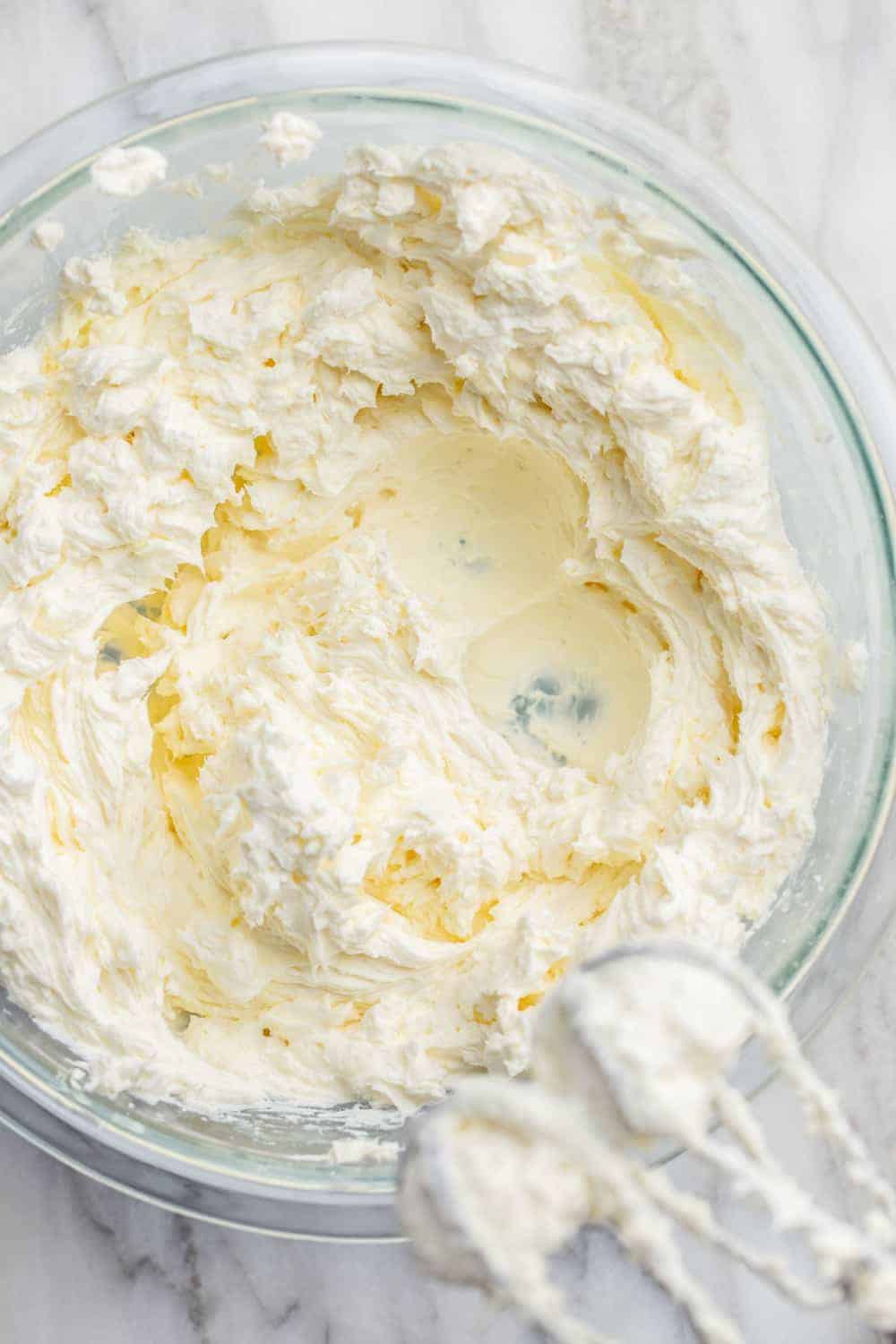 Softened cream cheese whipped with a hand mixer in a glass bowl
