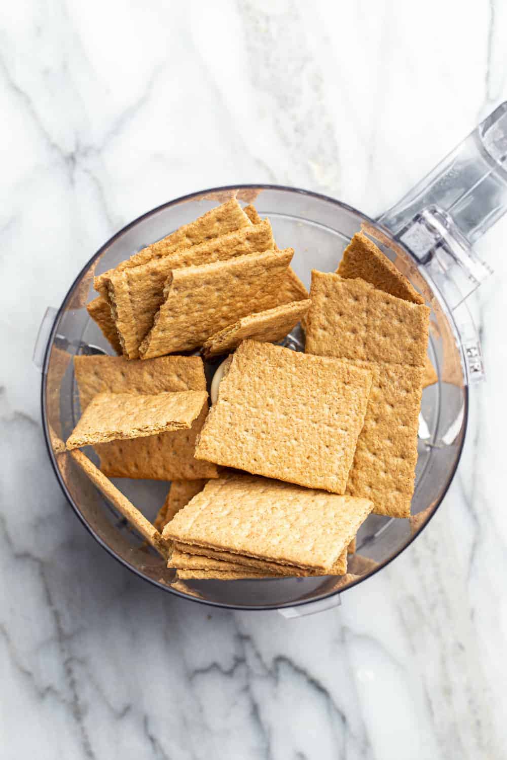 Graham crackers in the bowl of a food processor on a marble surface