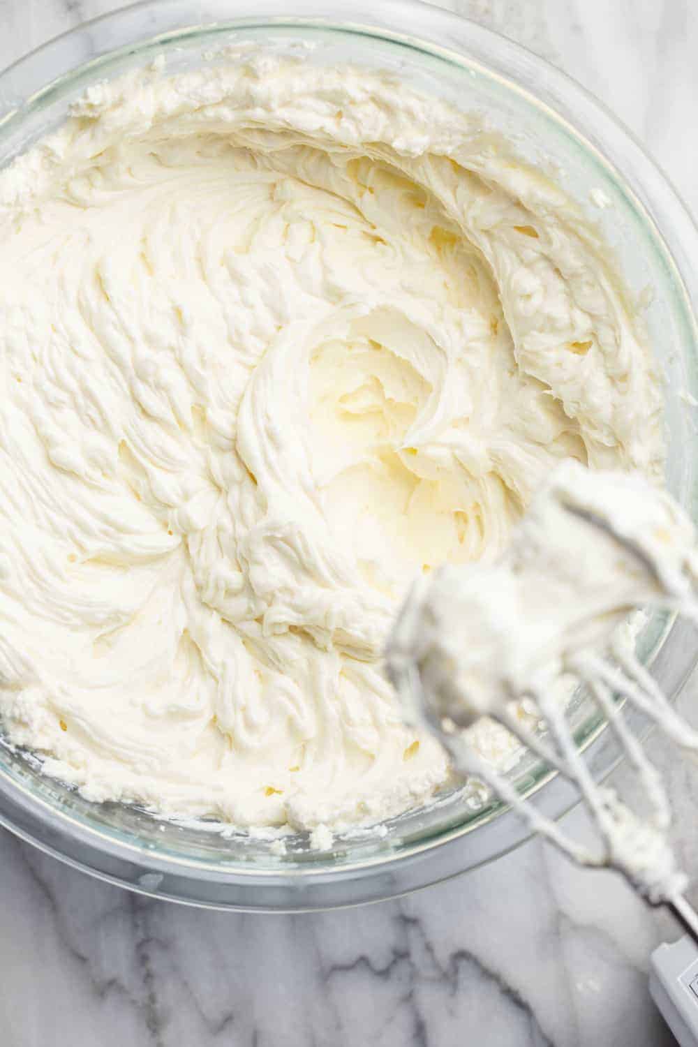 Electric mixer whipping cheesecake filling in a glass bowl