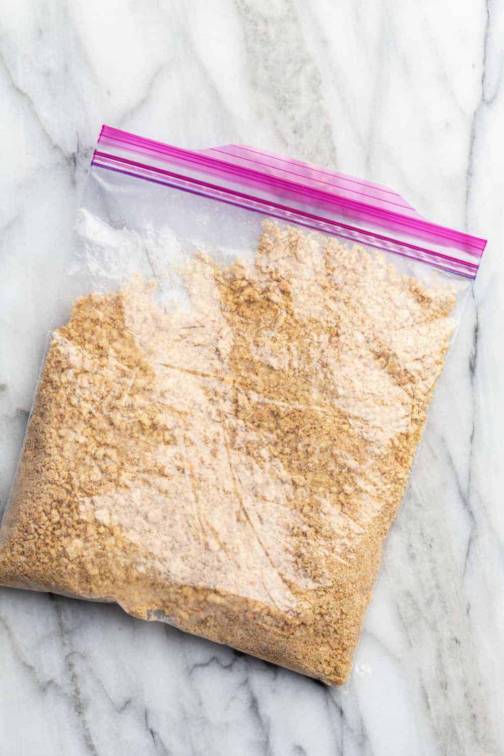 Zip-top bag of crushed graham cracker crumbs on a marble surface