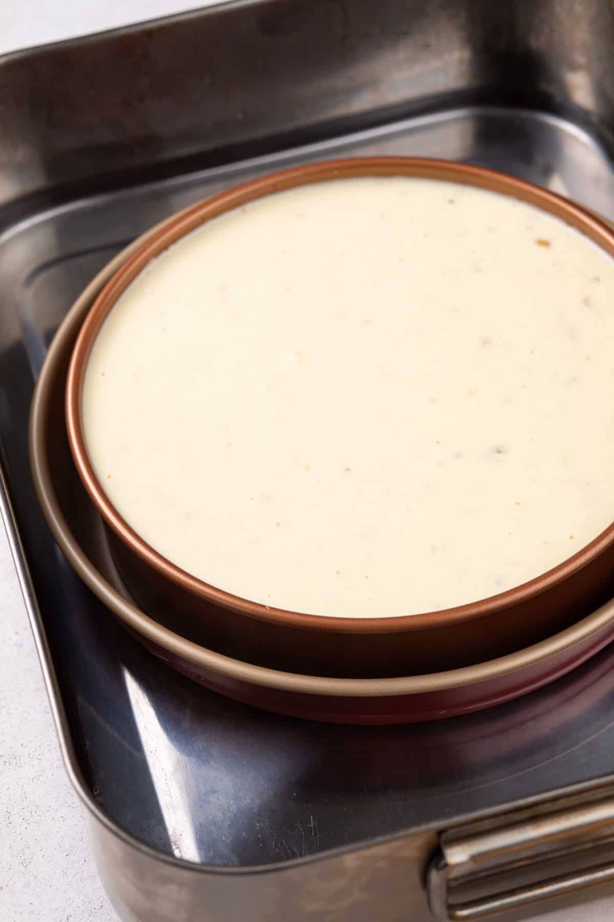 Cheesecake in a springform pan, set into a 10-inch cake pan and roasting pan for a water bath.