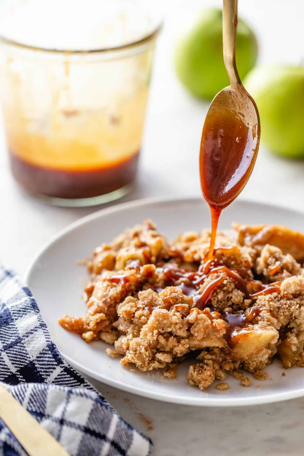 Spoon drizzling caramel sauce over a plate of caramel apple crisp