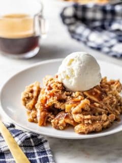 Caramel apple crisp topped with a scoop of vanilla ice cream on a white plate