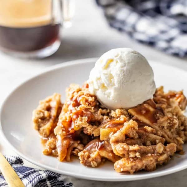 Caramel apple crisp topped with a scoop of vanilla ice cream on a white plate