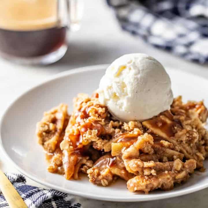Caramel apple crisp topped with a scoop of vanilla ice cream on a white plate