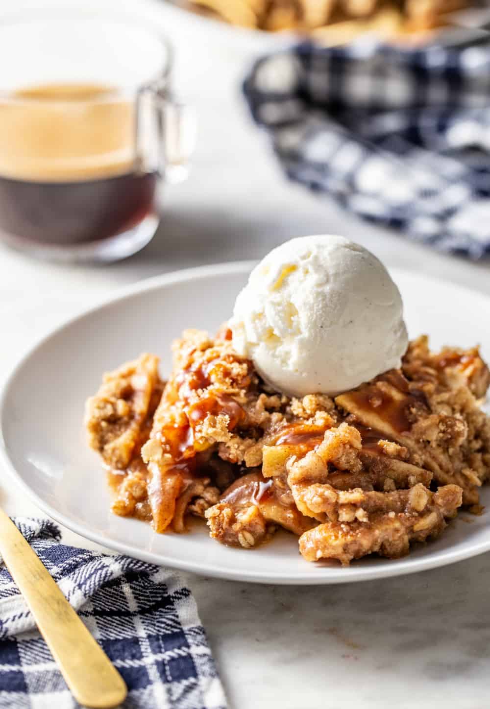 Caramel apple crisp topped with a scoop of vanilla ice cream on a white plate