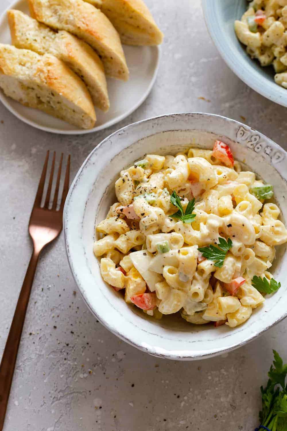 Bowl of macaroni salad next to a plate of sliced bread