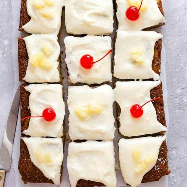 Pineapple cake topped with cream cheese frosting and cut into slices, topped with cherries and pineapple