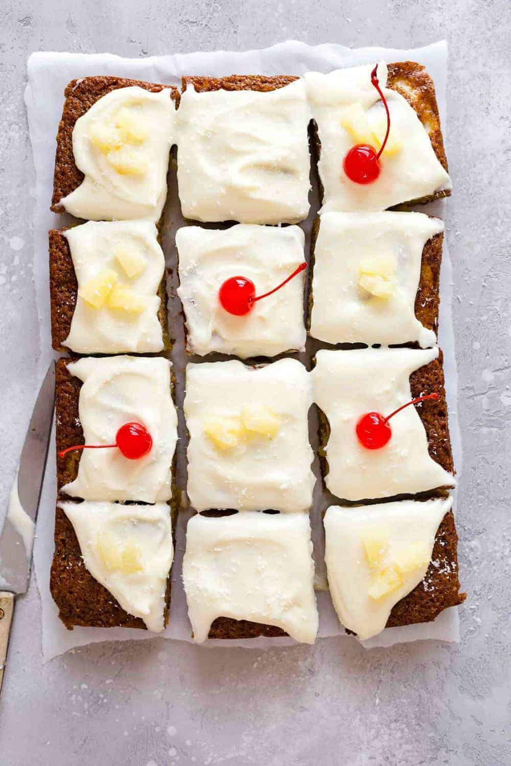 Pineapple cake topped with cream cheese frosting and cut into slices, topped with cherries and pineapple