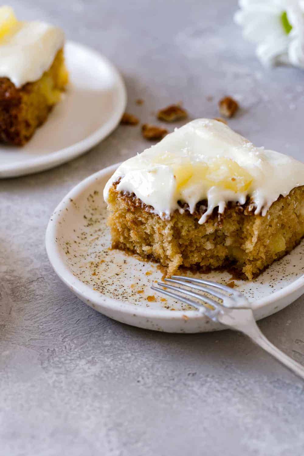 Close up view of a slice of pineapple cake topped with cream cheese frosting and pineapple