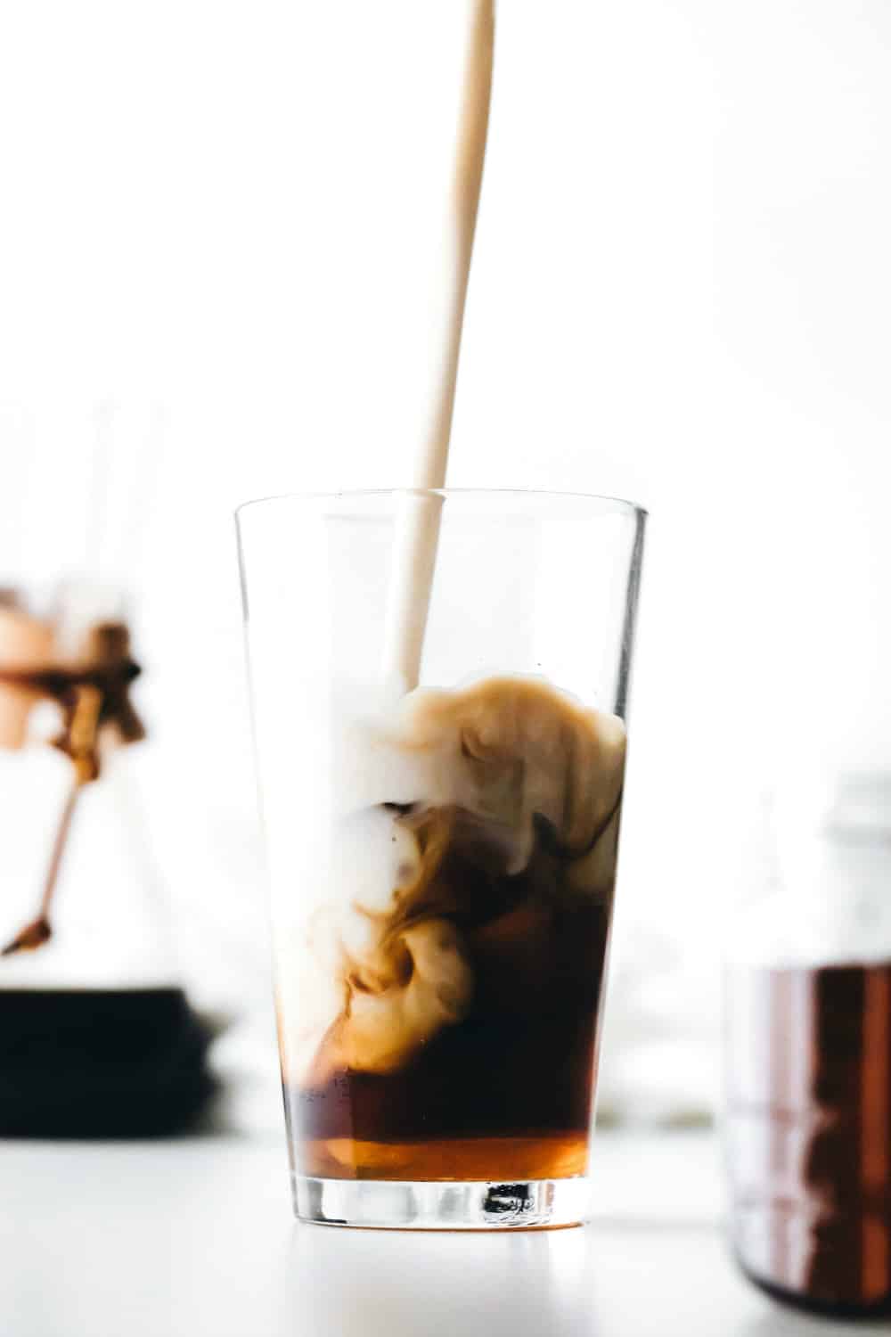 Milk being poured into a glass of iced coffee with vanilla coffee syrup