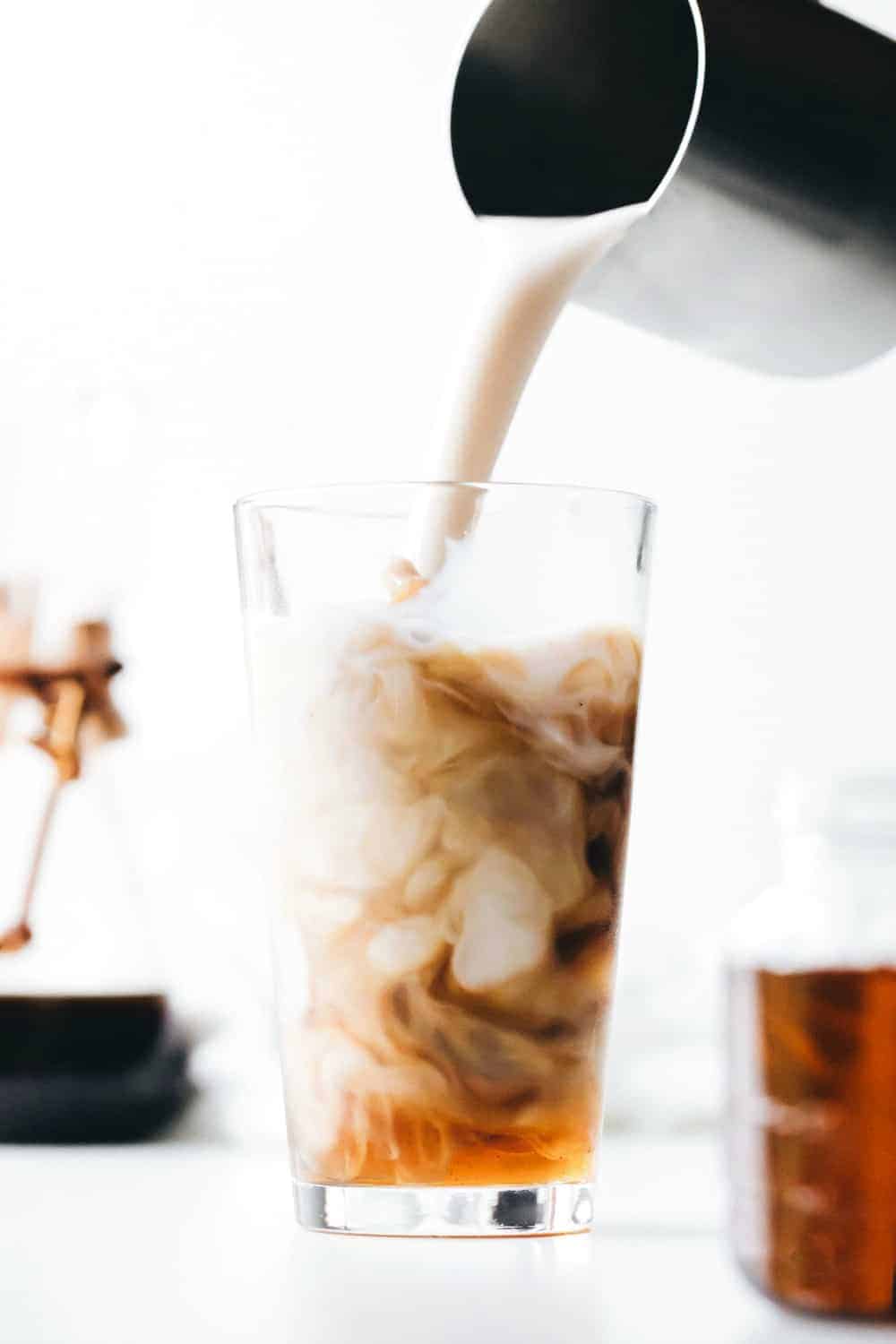 Pouring milk into a glass of iced coffee and vanilla coffee syrup