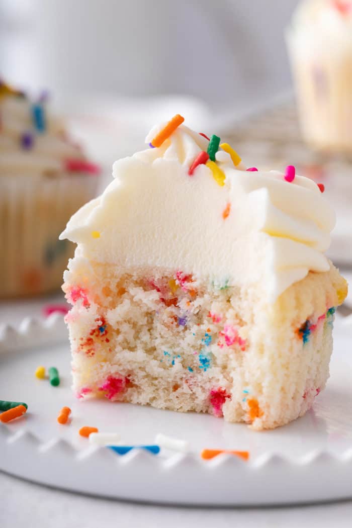 Funfetti cupcake with a bite taken out of it on a white plate.
