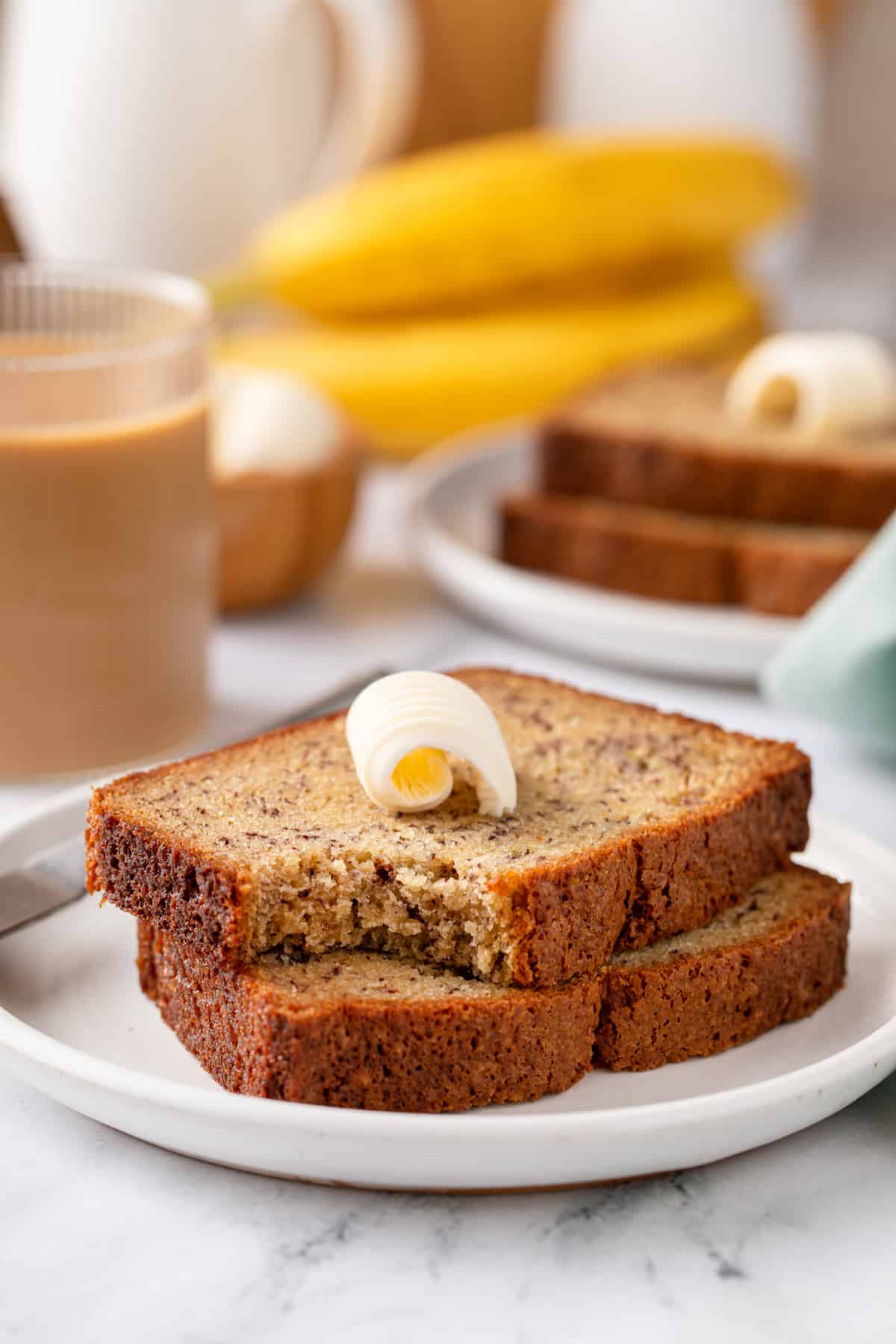 Two slices of banana bread stacked on a white plate. A bite has been taken from the corner of the top slice.