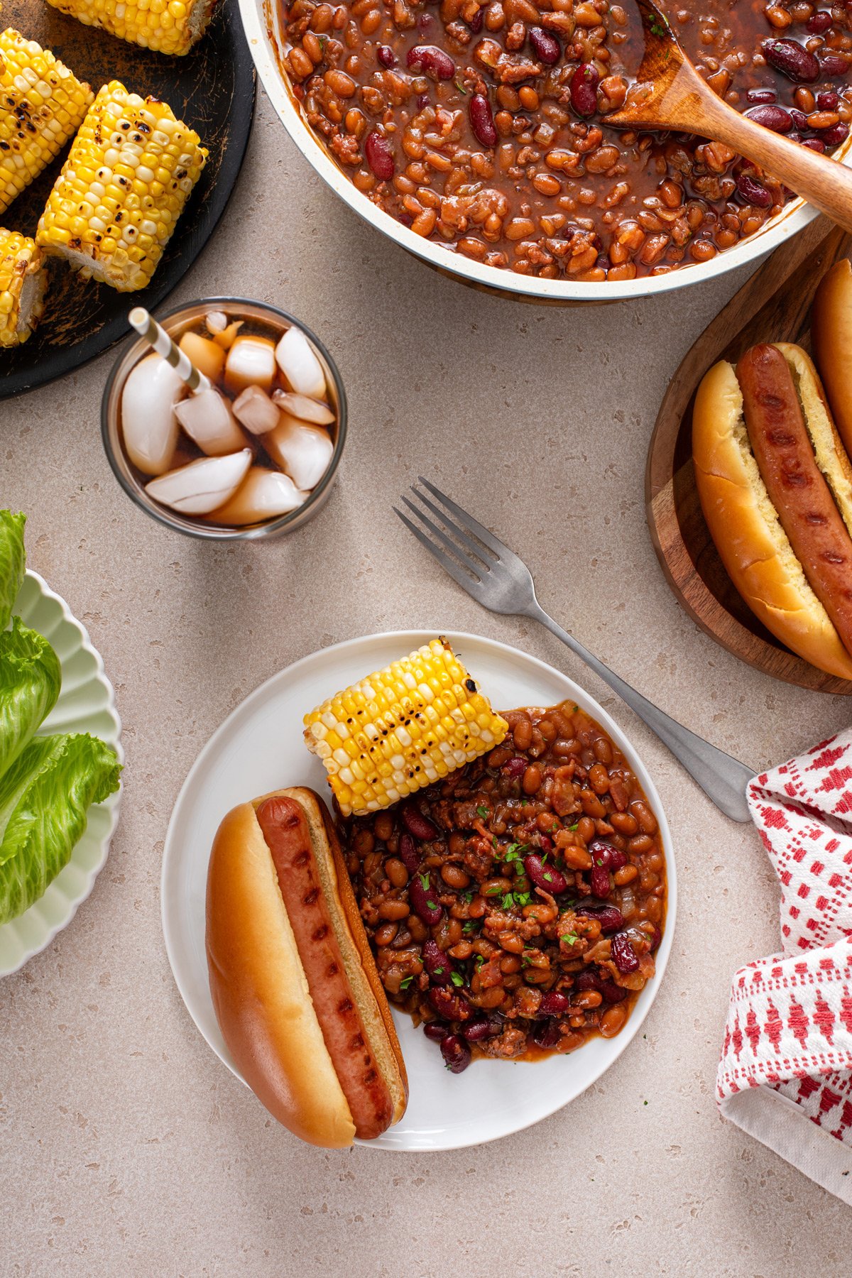 Overhead view of easy baked beans on a white plate with a hot dog and corn.