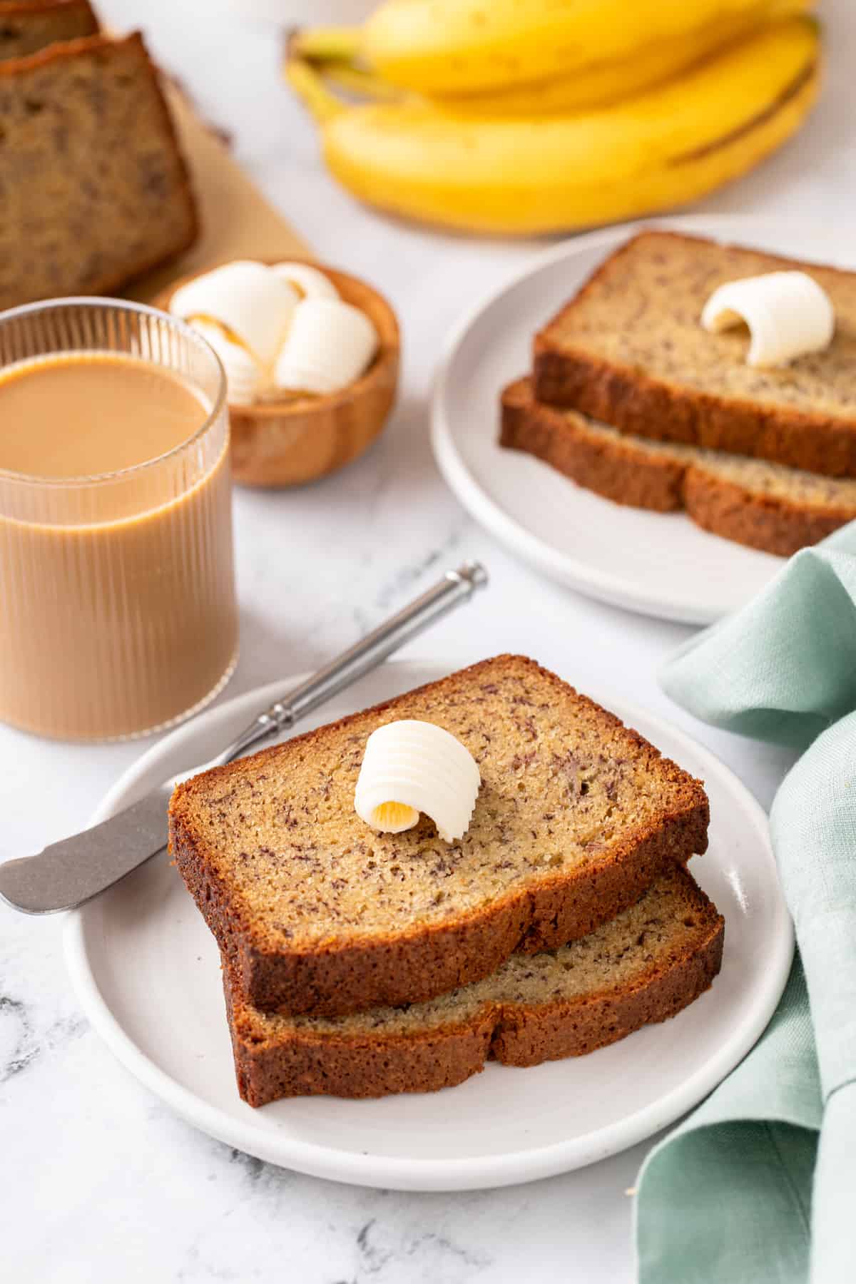 Two slices of dominique ansel's banana bread on a white plate, with a second plate of the bread in the background.