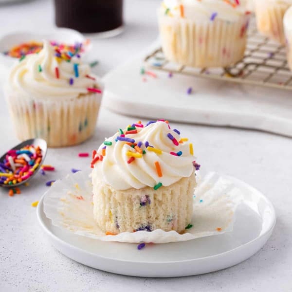 Unwrapped funfetti cupcake on a white plate.