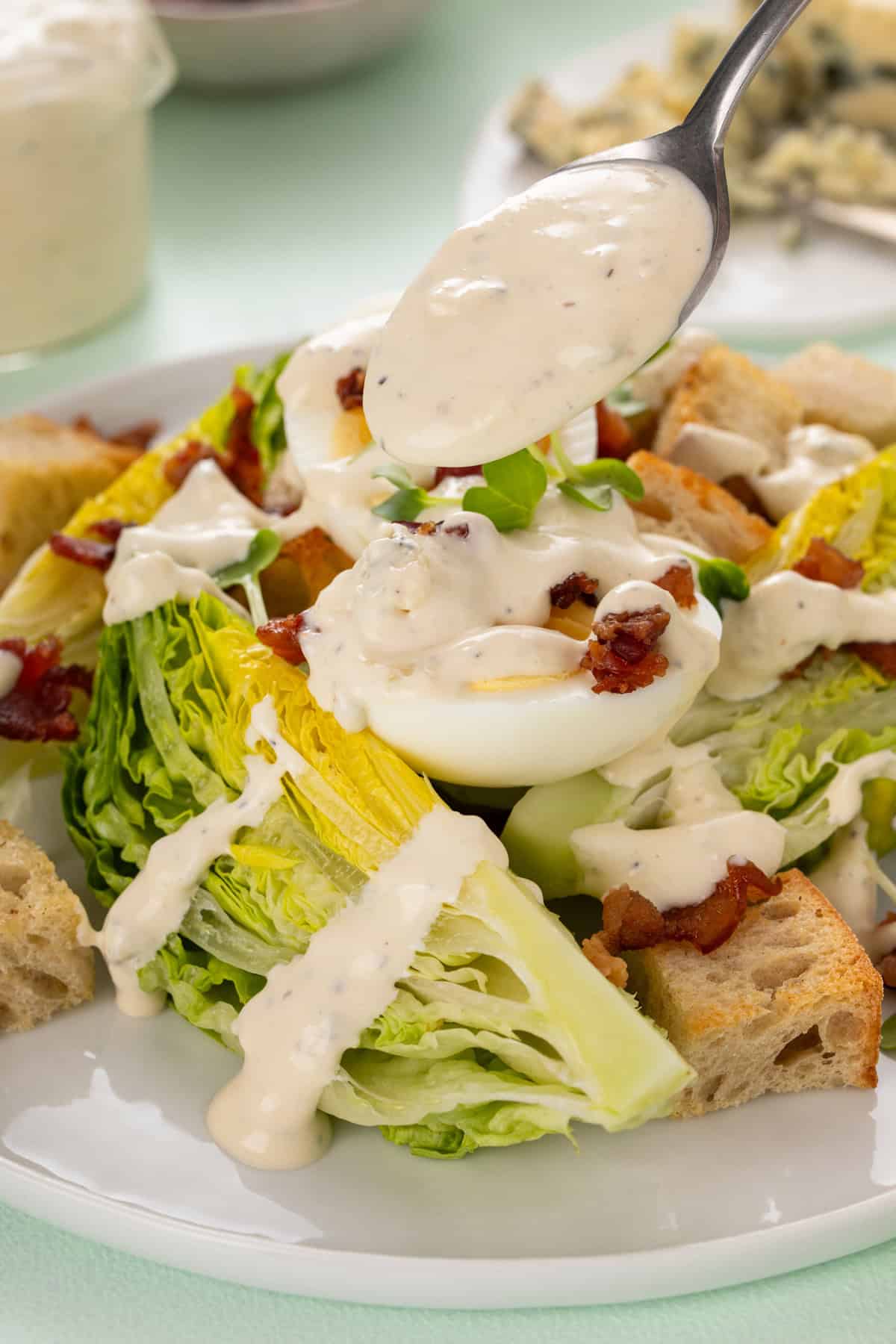 Spoon adding blue cheese dressing over a green salad on a white plate.