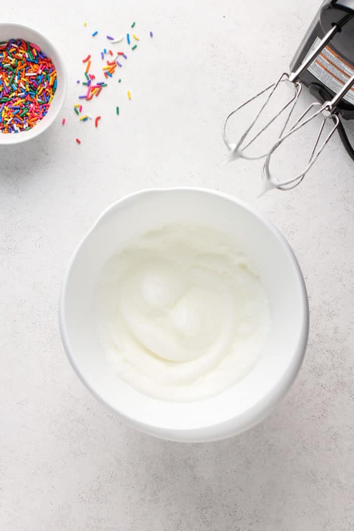 Whipped egg whites in a white mixing bowl.