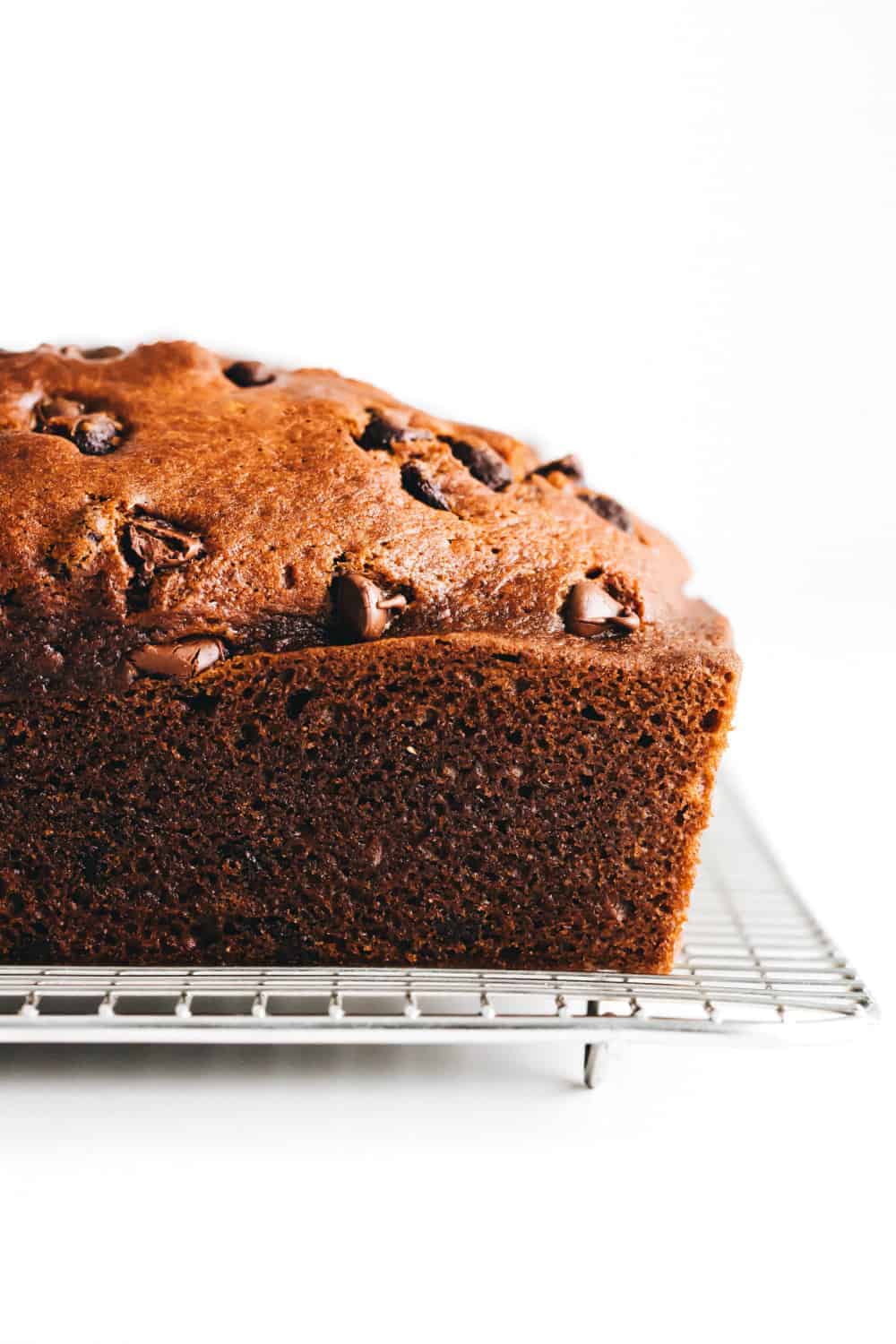 Side view of a loaf of pumpkin chocolate chip bread on a cooling rack