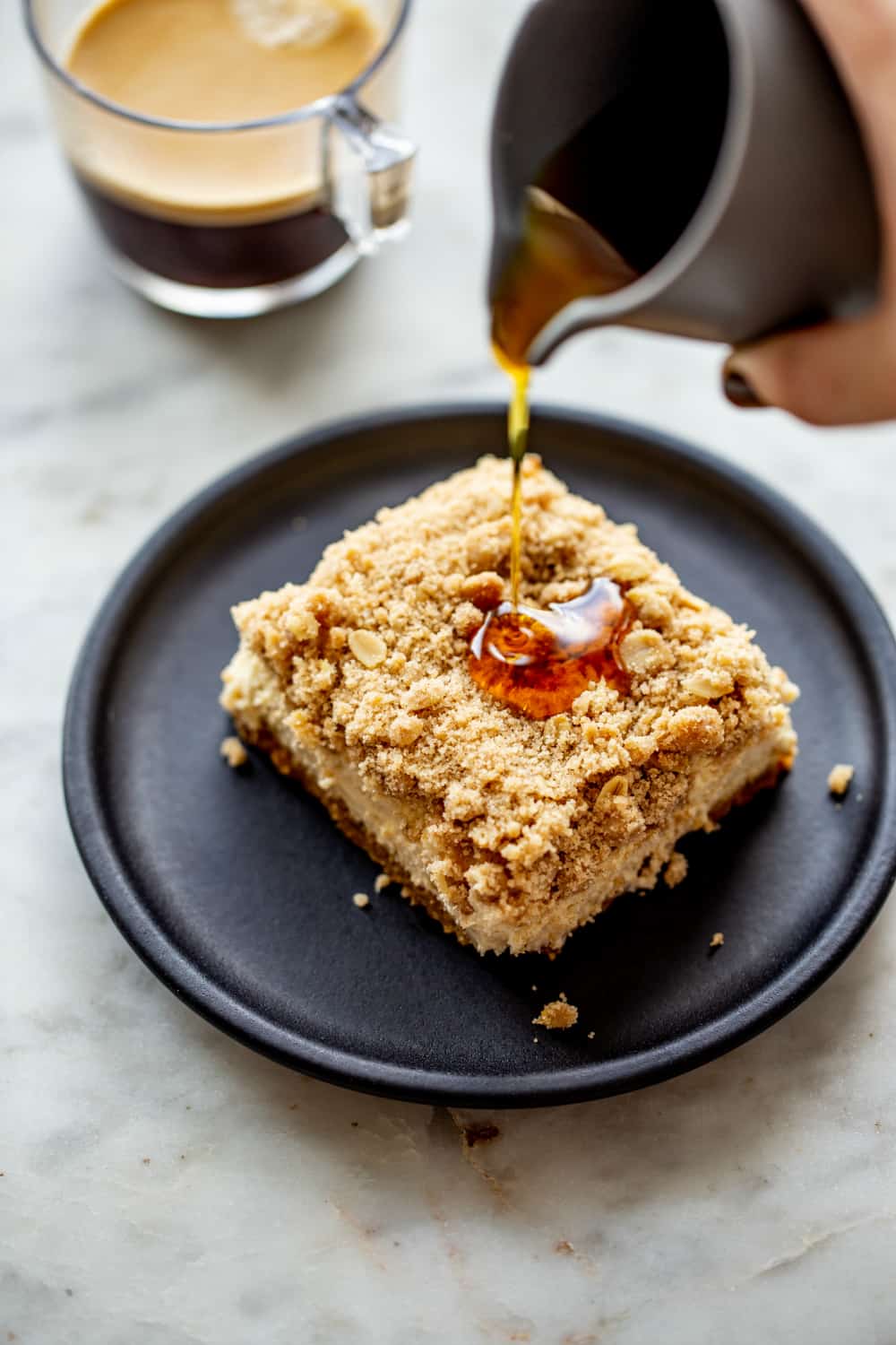 Maple syrup being poured over a slice of maple cheesecake bar on a plate