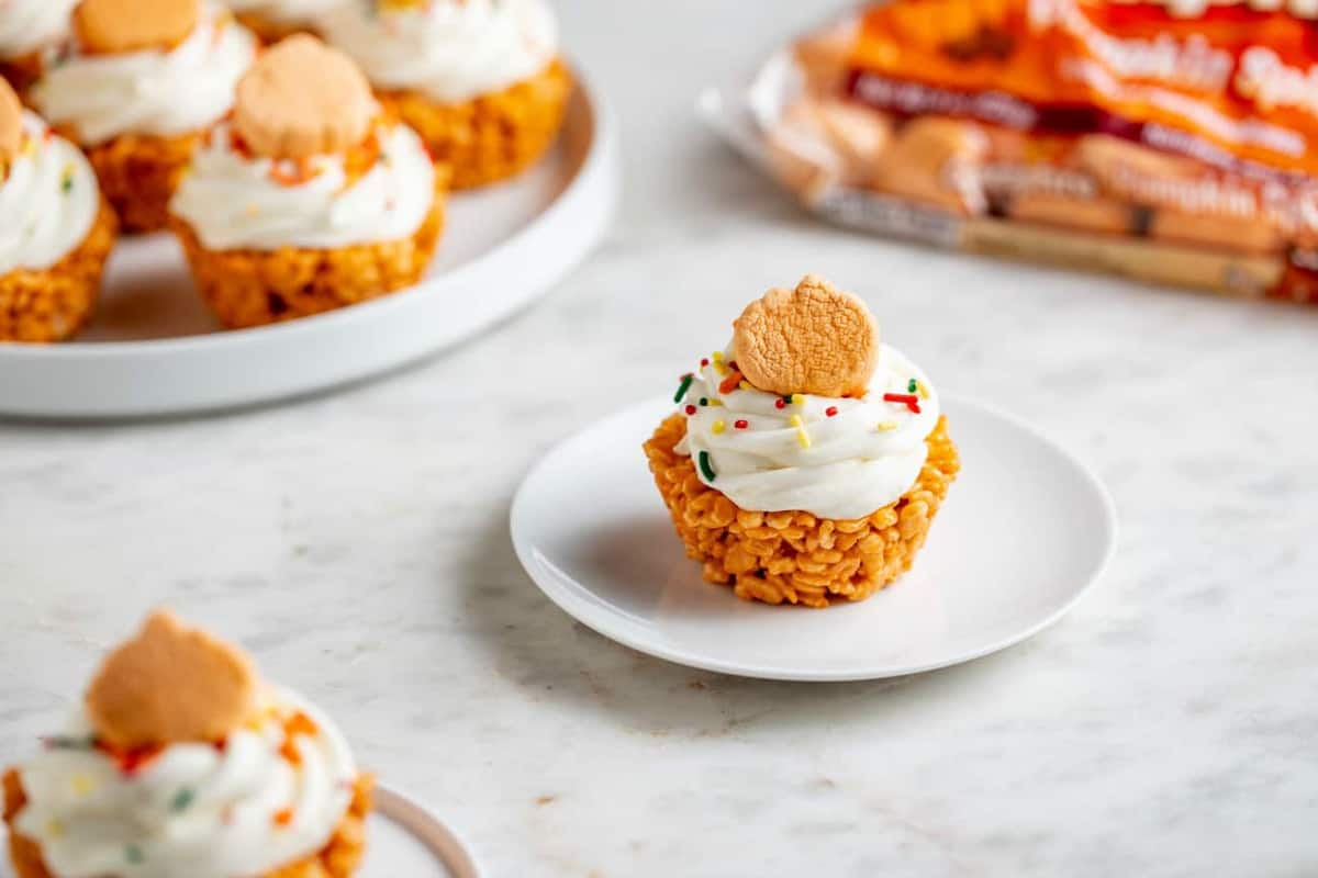Plated pumpkin spice marshmallow treat cupcake in front of a platter of marshmallow treat cupcakes