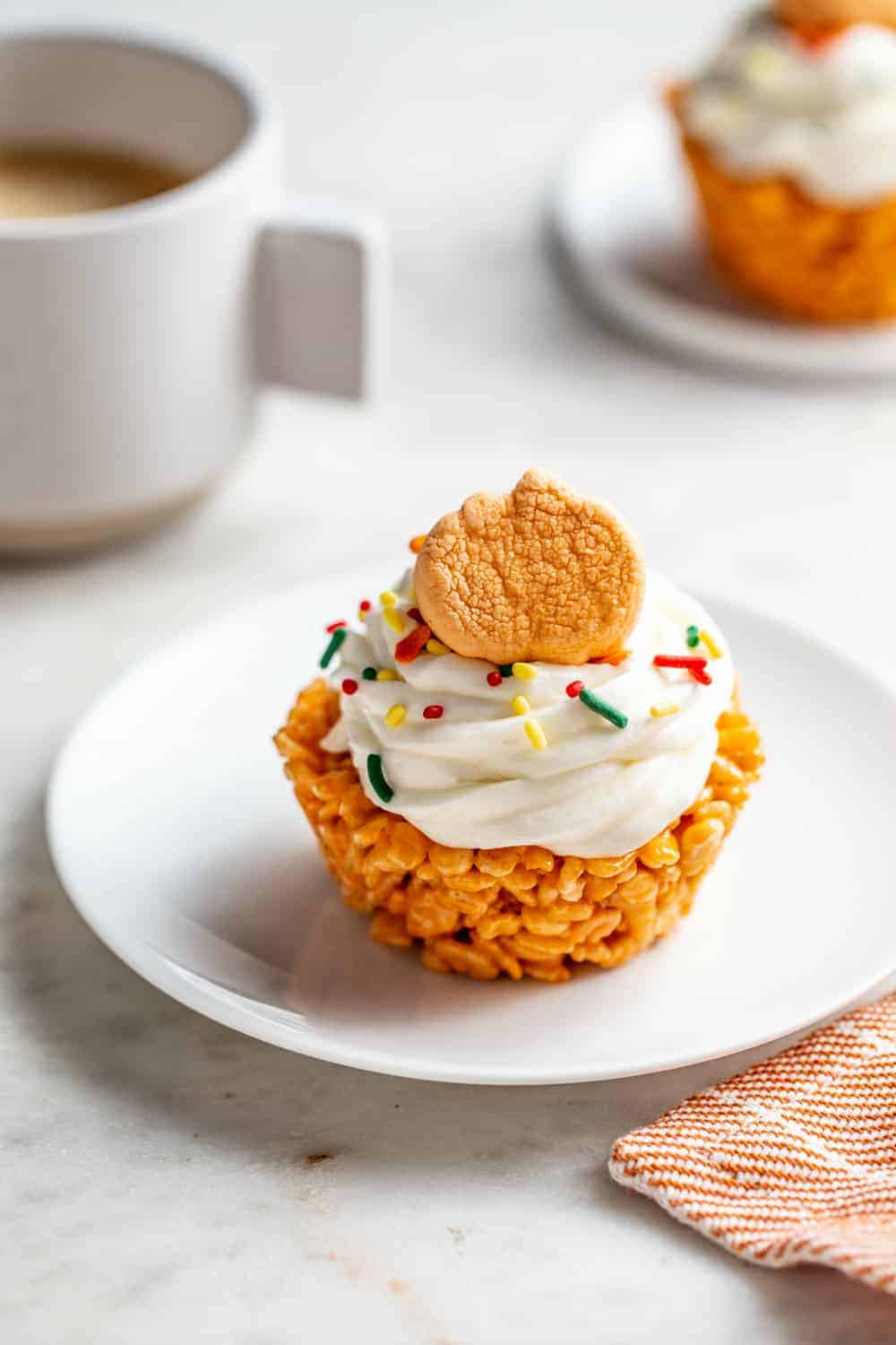 Pumpkin spice marshmallow treat cupcake on a white plate in front of a cup of coffee