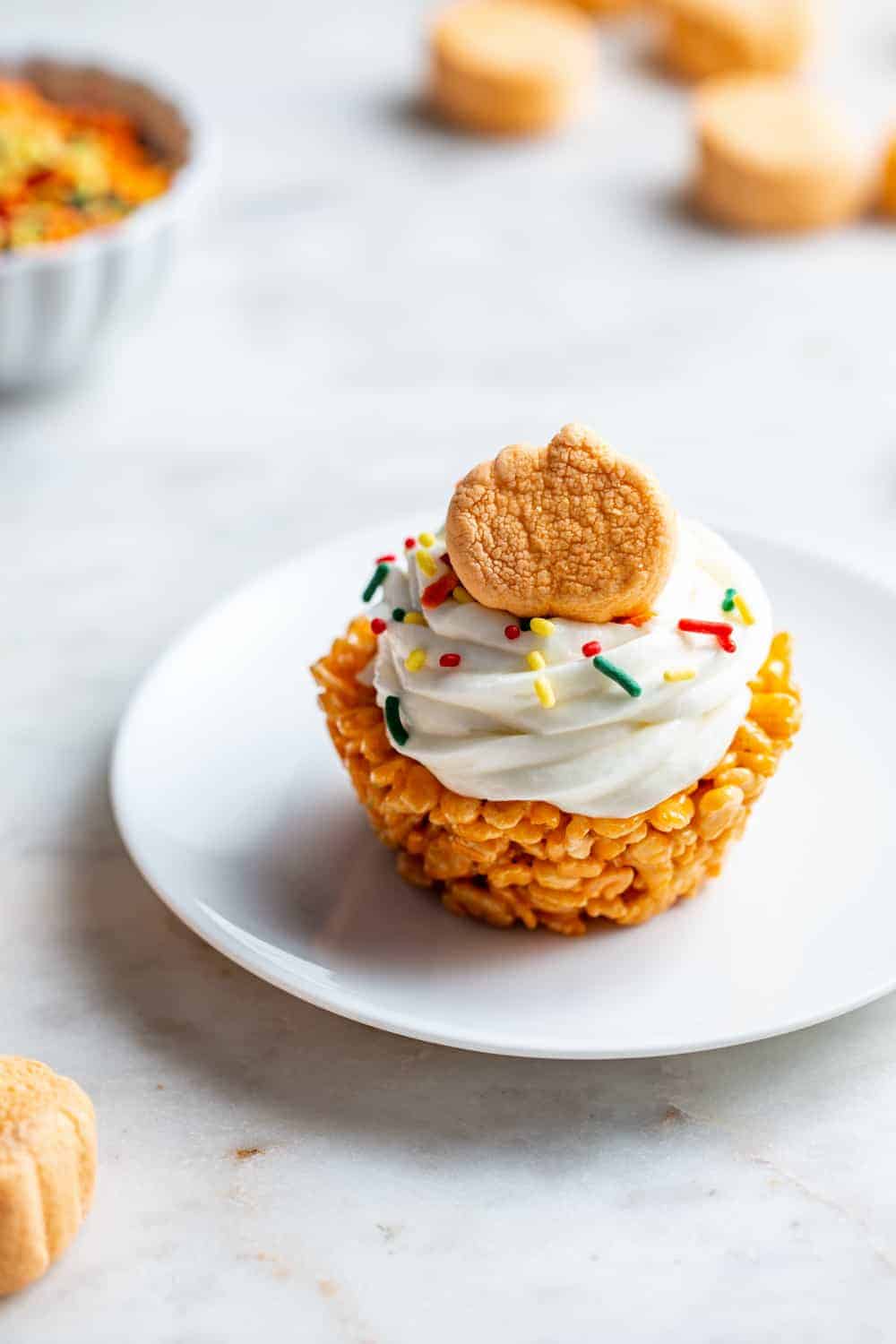 Plated pumpkin spice marshmallow treat cupcake with pumpkin spice marshmallows in the background