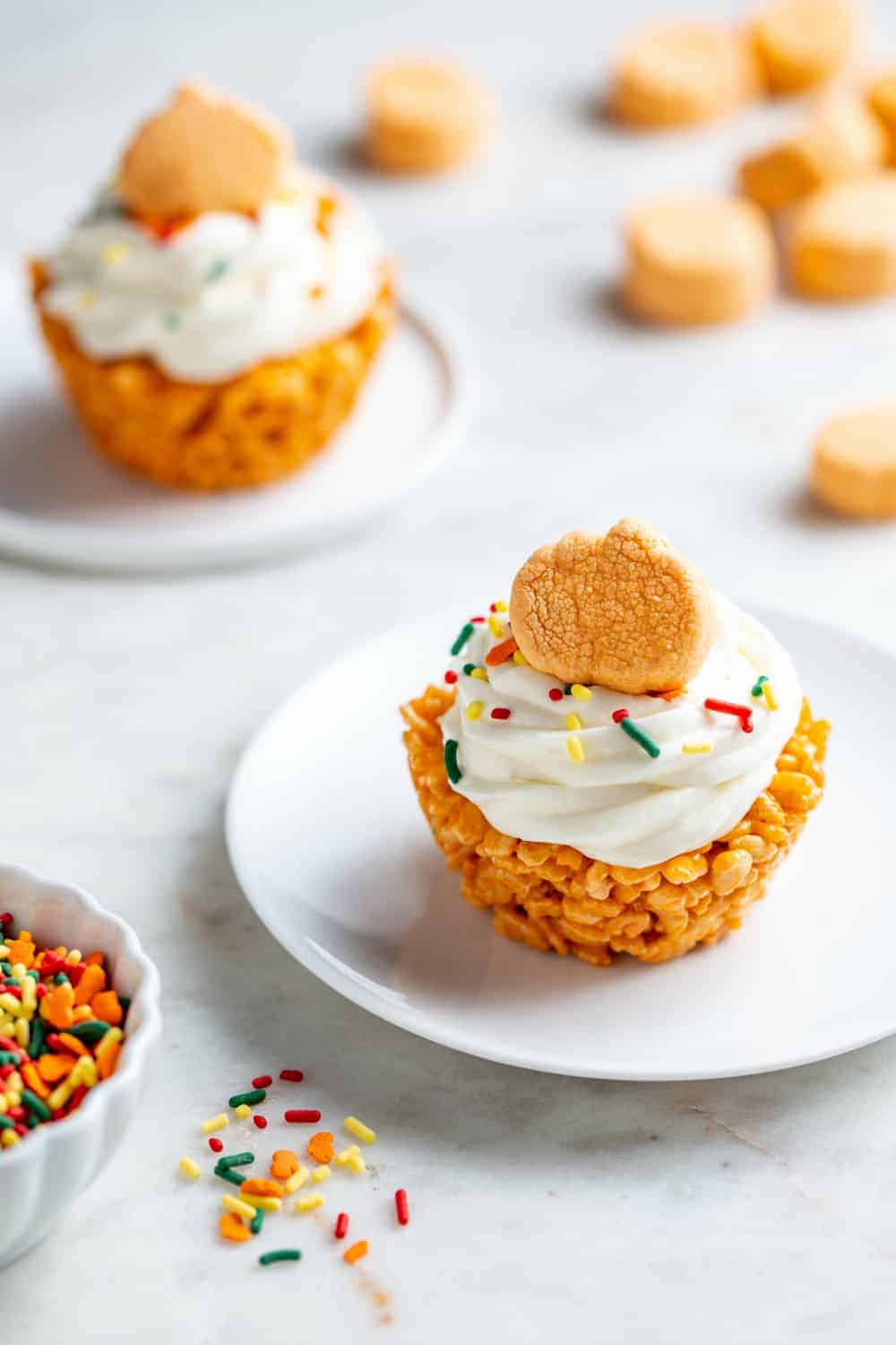 Two plated marshmallow treat cupcakes topped with pumpkin spice marshmallows