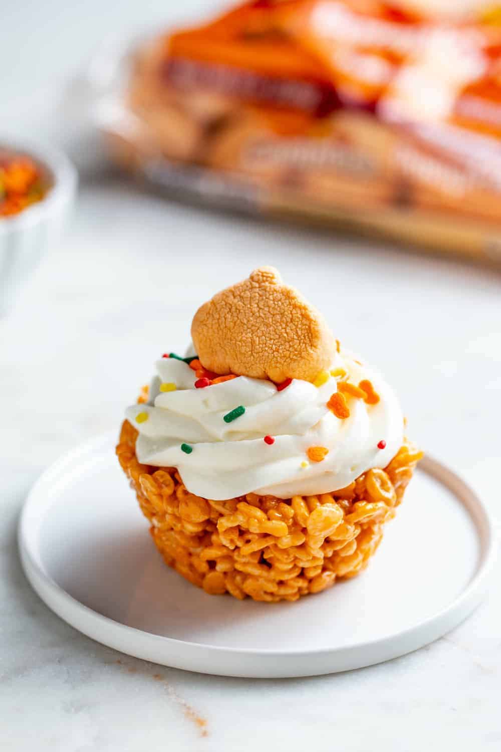 Plated marshmallow treat cupcake topped with a pumpkin spice marshmallow and sprinkles