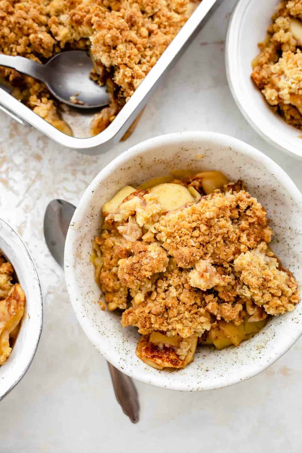 Pan of old fashioned apple crisp surrounded by small bowls of crisp