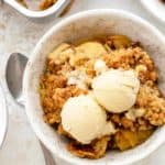 Spoon next to a small bowl of old fashioned apple crisp, topped with vanilla ice cream