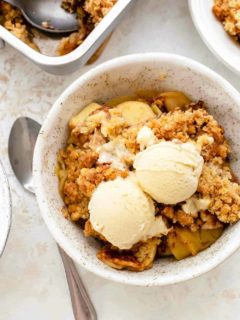 Spoon next to a small bowl of old fashioned apple crisp, topped with vanilla ice cream